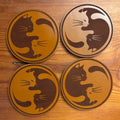 Four wooden coasters with cat designs on a wooden surface