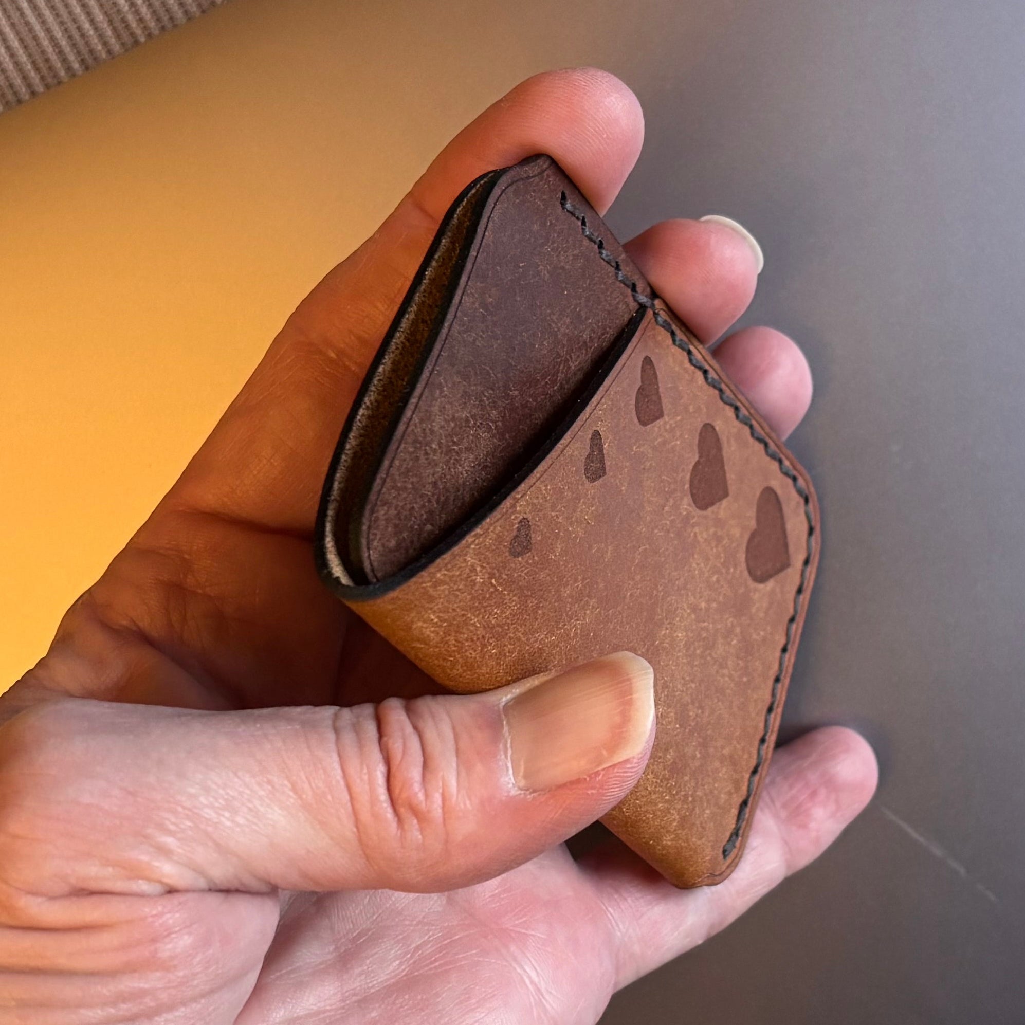 Hand holding a brown leather wallet in front of a laptop on a couch