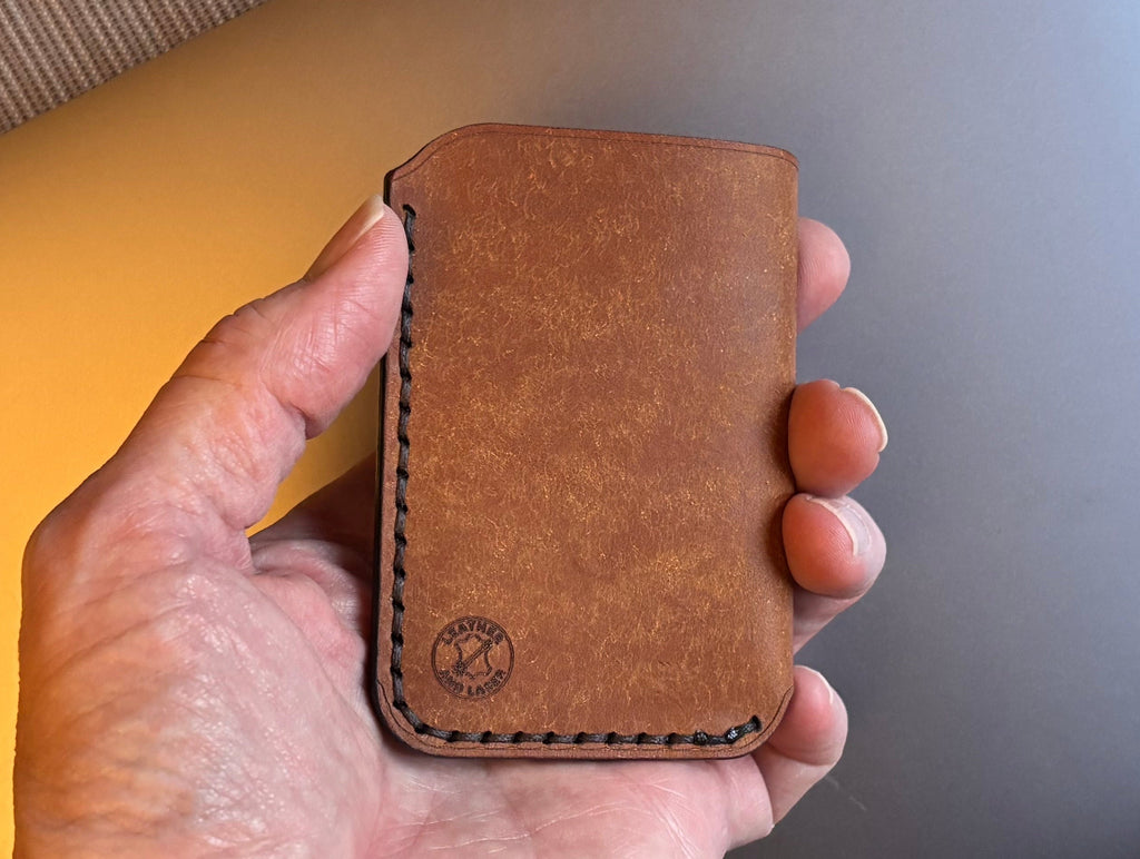 Hand holding a brown leather cardholder with a laptop in the background