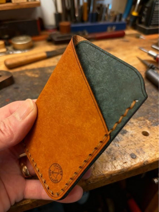Handmade leather wallet held by a person with a workshop background