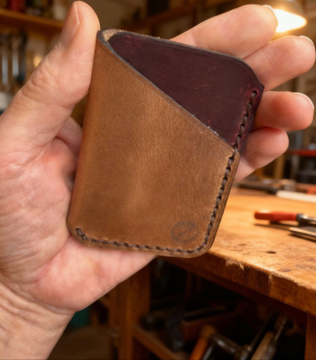 Hand holding a brown leather wallet with a blurred workshop background