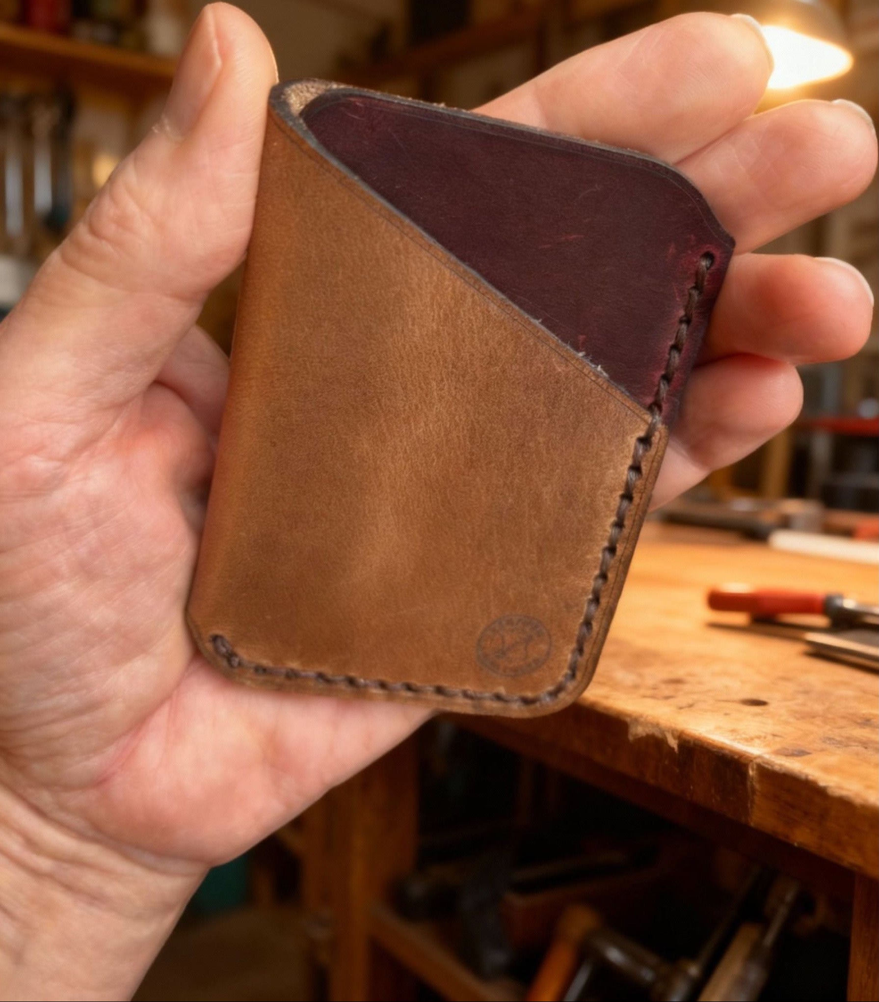 Hand holding a brown leather wallet with a blurred workshop background